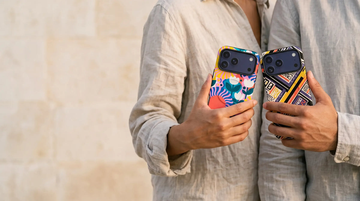 Two people side by side holding iPhones in Finnaij cases: a Nordic floral design by Salla Niemi and Danfo After Dark by Ada Okoye